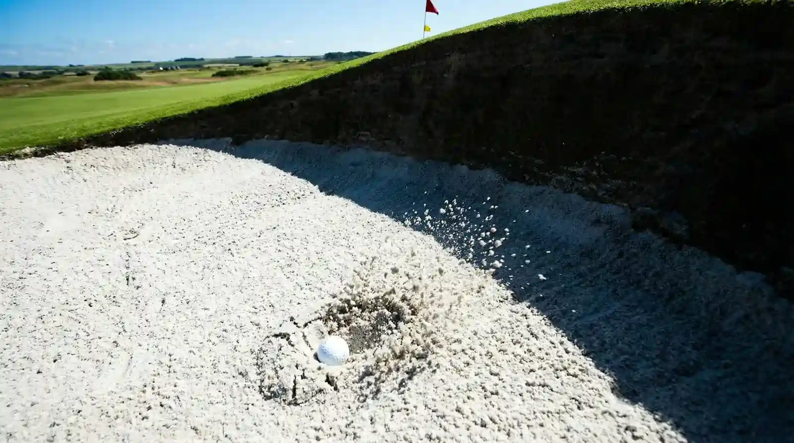Bola de golf en un bunker profundo con arena salpicando tras un golpe fallido